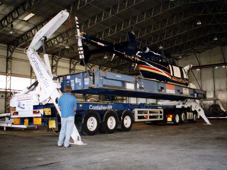 Helicopter loaded onto truck bed inside a giant warehouse