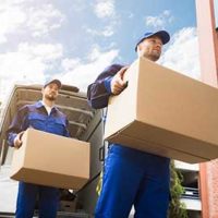 Men in blue uniforms carrying boxes from moving truck to building